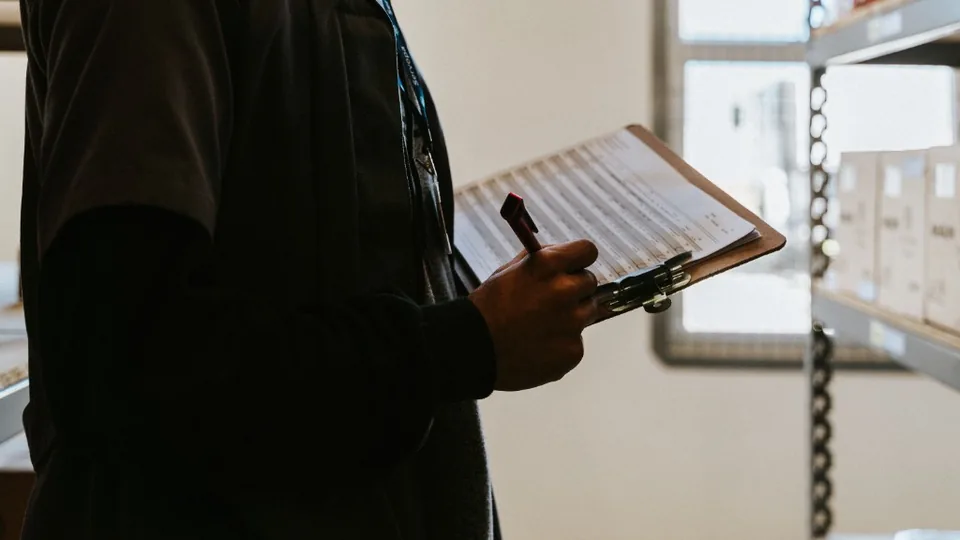 Worker recording inspection notes on a clipboard in a warehouse